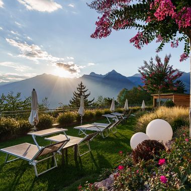 Eine von der Sonne durchflutete Hotelterrasse mit Liegestühlen auf einem gepflegten Rasen vor einer imposanten Bergkulisse bei Sonnenuntergang.