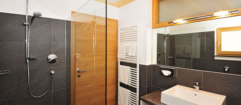 Bagno moderno con doccia a parete, lavabo rettangolare, asciugamani bianchi e porta in legno.