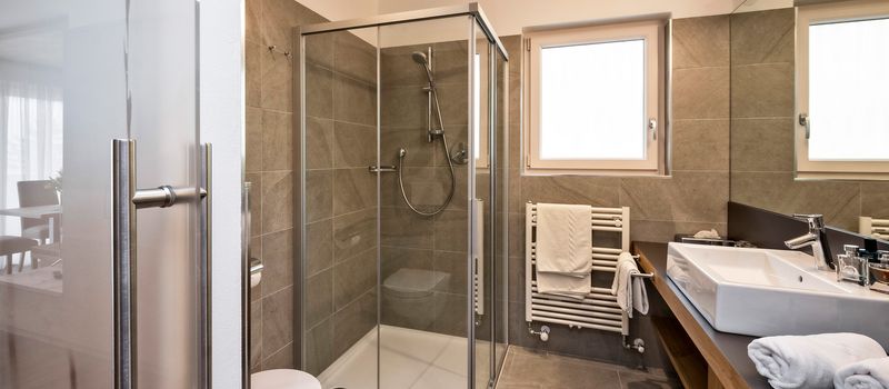 Bagno moderno con doccia in vetro, lavabo, asciugamani e finestra