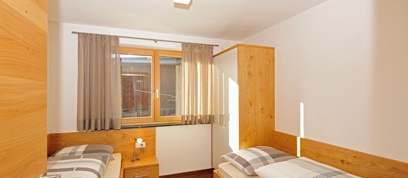 Camera da letto con due letti singoli, armadio bianco e finestre con tende beige.