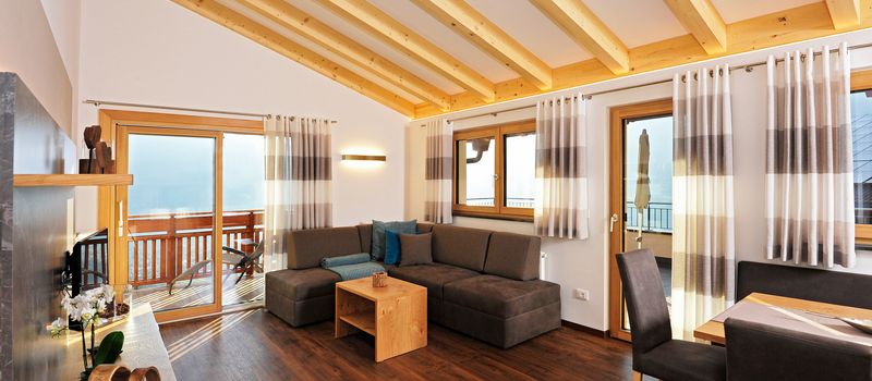 Soggiorno moderno con soffitto con travi in legno, divano grigio, tavolino e porta finestra con vista balcone.