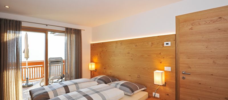 Camera da letto moderna con letto matrimoniale, parete attrezzata in legno, e porta finestra con balcone.