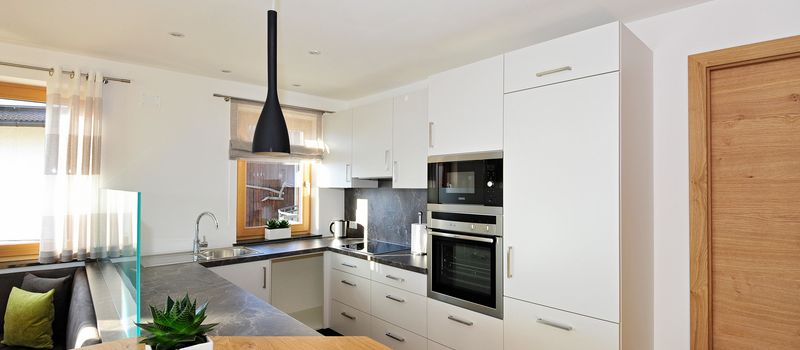 Cucina moderna bianca con piano di lavoro grigio e tavolo in legno con pianta verde.