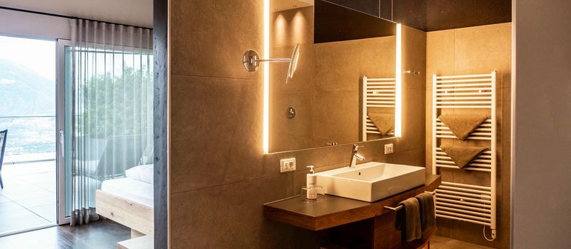 Modernes Badezimmer mit beleuchtetem Spiegel und Waschbecken, angrenzend an Schlafzimmer mit Balkon.