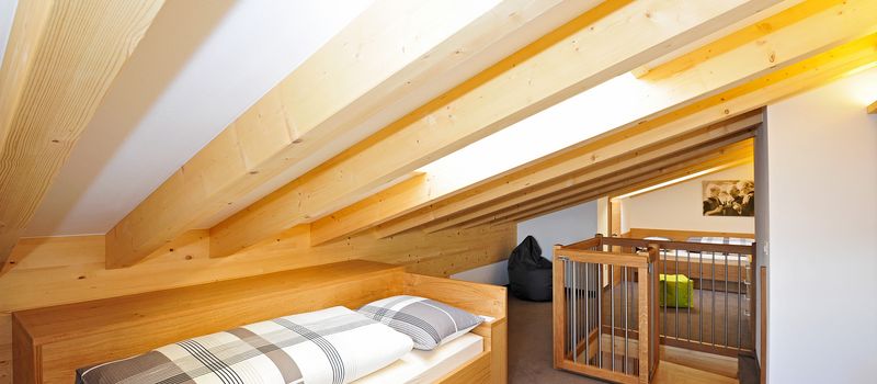 Camera mansardata con travi in legno chiaro, letto singolo e scala con cancello di sicurezza.