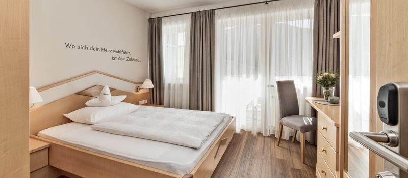 Camera da letto luminosa con letto matrimoniale, scrivania, sedia e finestra con tende.