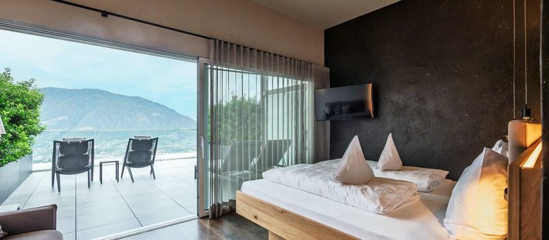 Camera moderna con letto matrimoniale, TV a parete e terrazza con vista sulle montagne.