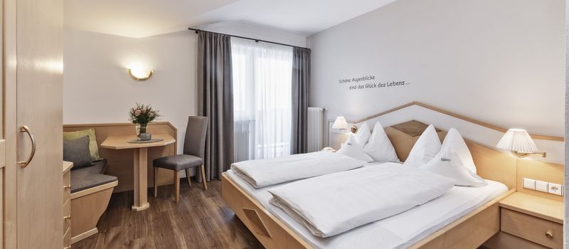 Camera da letto moderna con letti doppi, tavolo con sedie e finestra con tende grigie.