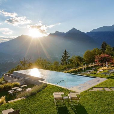 Ein Infinity-Pool auf einer grünen Wiese vor einer Gebirgslandschaft bei Sonnenuntergang.