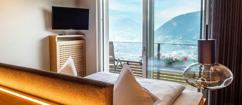 Camera da letto moderna con letto, TV, lampada e balcone con vista sulle montagne.